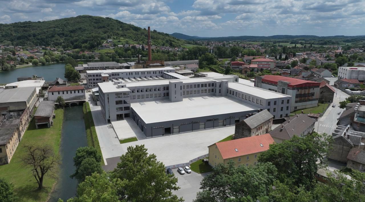 Luftaufnahme des Areals mit Bürotrakt, Hallen und Fluss