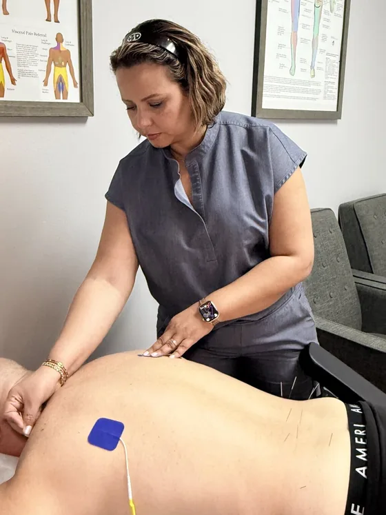 Dr. Zakia Chang treating a patient with electro-acupuncture, nerve pain charts on the wall