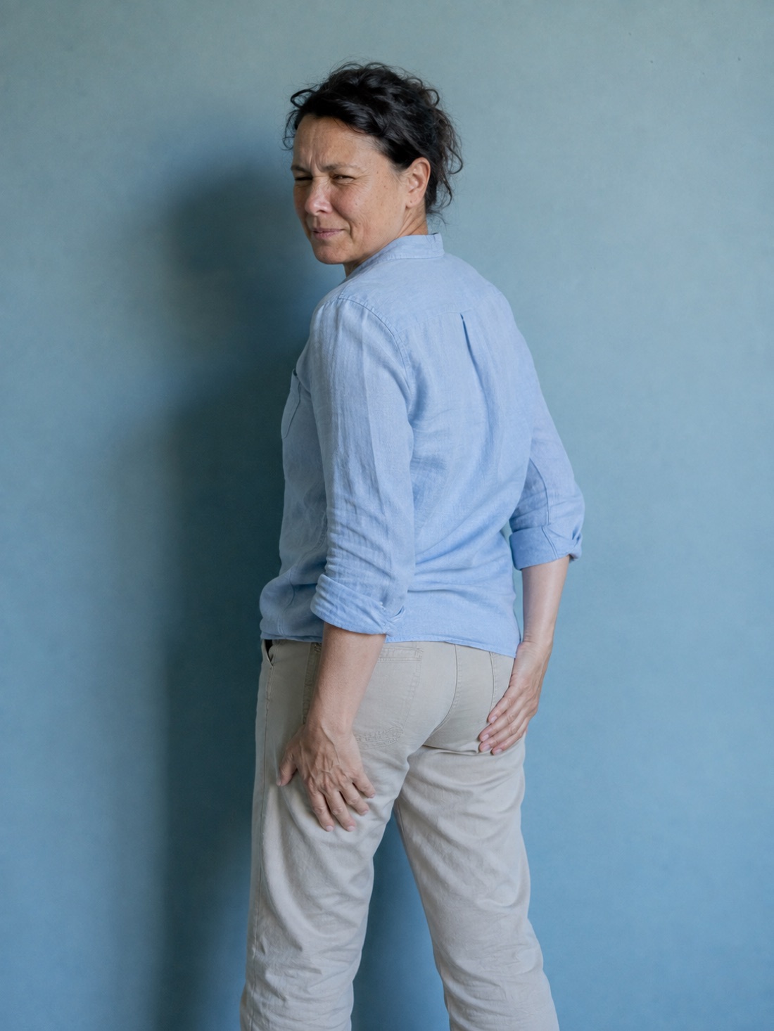 The same woman standing turned away, one hand pressed against the back of her upper thigh